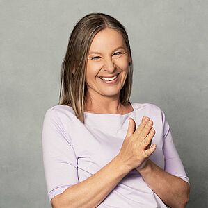 Portrait zeigt herzhaft lachende Frau die Hände verschließt.